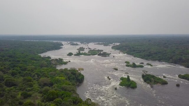 Nile River in Uganda flowing through Murchison Falls National Park, showing whitewater rapids, scattered green islands, and dense tropical forest stretching to the horizon, drone pand and reveal.