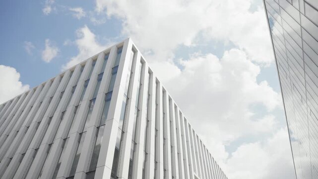 Dynamic shot of a modern building with sleek, vertical lines set against a partly cloudy sky. The light highlights the structure's geometry, offering an impressive architectural view.