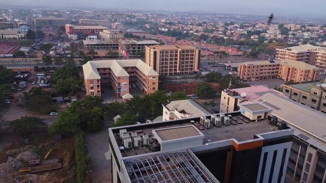 Aerial of a rooftop of a new office building overlooking the beautiful and large city of Abuja, Nigeria. Birds frantically fly in front of the camera while the drone flies backwards