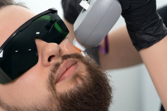 Young bearded man getting laser facial treatment by professional cosmetologist in a beauty clinic. Healthy man lifestyle concept