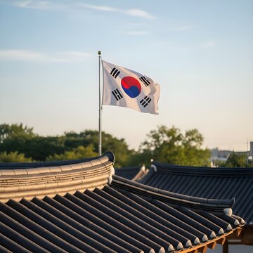 전통적인 한국 기와지붕 너머로 푸른 하늘 아래 당당하게 펄럭이는 태극기가 애국심과 전통의 미를 보여주는 풍경 / A scenery showing patriotism and traditional beauty with the Korean flag fluttering proudly under the blue sky over a traditional tile ro