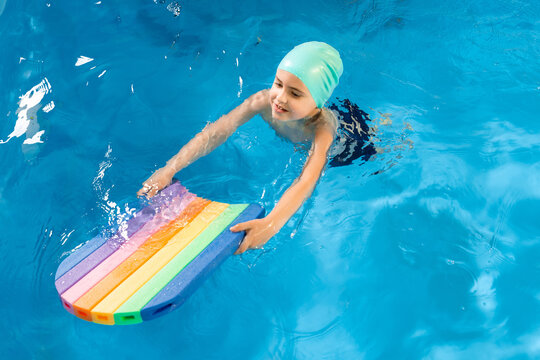 Swimming class. Close up of kids practicing flutter kick with kick board in swimming pool