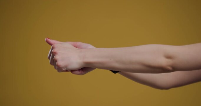 Close up of a young woman's clasped hands with red nails against a yellow background