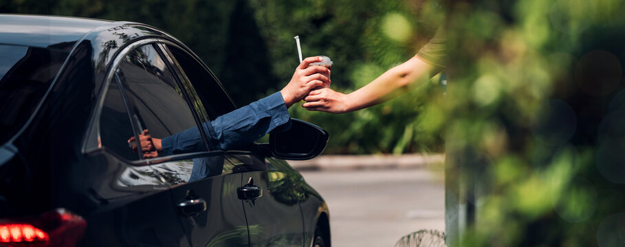 Hand Man in car receiving coffee in drive thru fast food restaurant. Staff serving takeaway order for driver in delivery window. Drive through and takeaway for buy fast food for protect covid19.