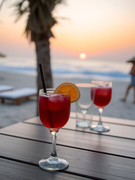 Tasty red cocktail with orange slices placed on wooden table with glass goblets on Fuseta Beach at sunset in summer