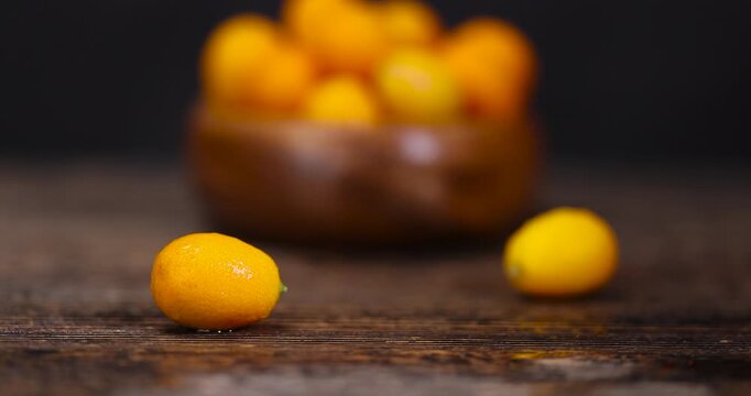 wet small orange fruits of juicy fresh and fragrant kumquat on a black wooden table, oval kumquat fruit covered with drops of water and scattered on a black table made of pine wood