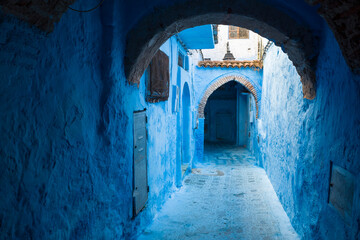 Naklejka premium Peaceful blue alley in Chefchaouen medina, Morocco, with arched doorways, cobblestone path, and traditional charm in a serene setting