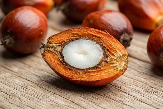 Halved oil palm fruit showing white kernel and orange mesocarp on wooden surface