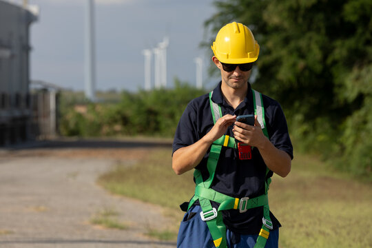 Engineer using smartphone during field operations at wind farm, highlighting safety, modern communication, clean renewable energy management in professional outdoor work.