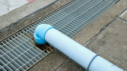 Roadside drainage channel with a steel grate cover and a large PVC pipe connected from the roof for effective rainwater discharge,