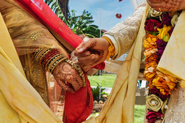 Indian Bride and Groom Holding Hands During Hindu Marriage Ritual gold bridal jewelry, and floral garlands