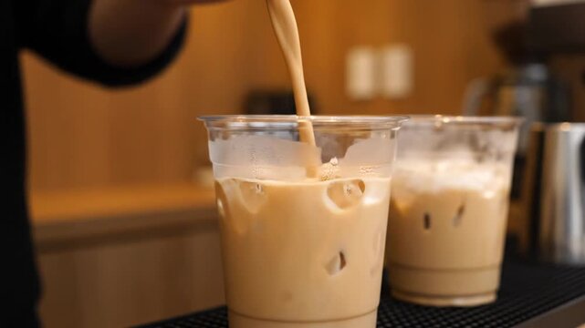 Iced coffee being poured into a clear plastic cup with ice, creating a refreshing beverage experience