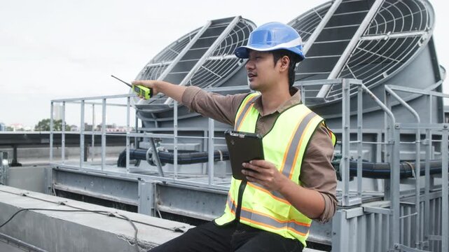 Two construction engineers in safety gear examine industrial HVAC units on rooftop, pointing and discussing project progress and setup.