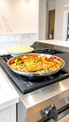 A vibrant dish of grilled fish and colorful vegetables sits on a stainless steel cooktop, near a bowl of pasta