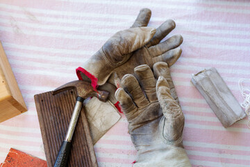 Still life of leather work gloves with small hammer and pieces of worn sandpaper