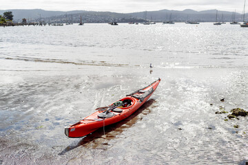 Single person sea kayak sitting on the sand at low tide on the Derwent river in Hobart