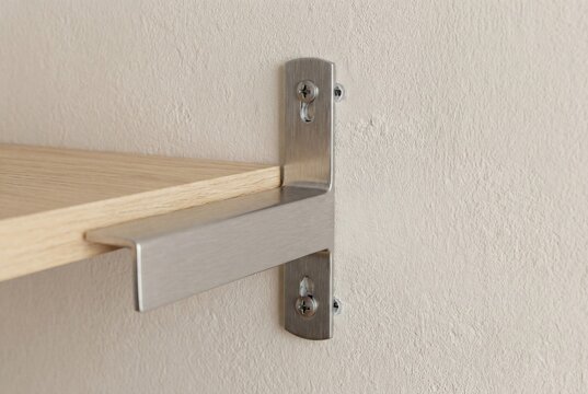 Close-up of poorly installed floating shelf bracket with misaligned wall holes, uneven screw placement, and visible surface damage on textured interior wall
