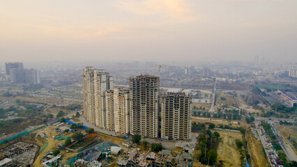 Fototapeta premium drone view of high-rise residential buildings under construction with crane in Gurgaon with hazy skyline, highlighting urban growth, real estate development, and air pollution.