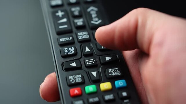 Close-up of a hand pressing the center OK Select button on a TV remote navigation pad, confirming a choice in an on-screen menu with shallow depth of field.