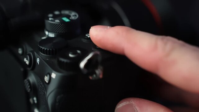 Finger presses the red record button on a mirrorless camera, starting video capture in moody studio lighting with shallow depth of field for creator tech b-roll.