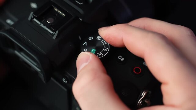 Close-up of hand turning the mode dial on a mirrorless camera, switching shooting modes in studio light with shallow depth of field for creator tech b-roll.