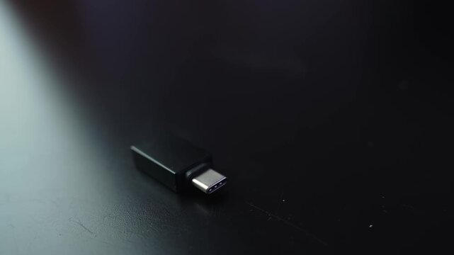 Macro shot of a USB-C to USB 3.0 adapter on a dark desk with shallow depth of field and copy space, ideal for tech connectivity, data transfer, and device compatibility b-roll.