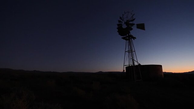 Water pump windmill blades turn slowly in blue twilight sky, copy space