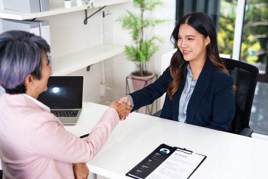 employer hr with employment contract job on desk officer hiring welcoming female asian newcomer worker manager shaking hands in contemporary office. Getting new job handshake concept.
