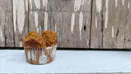 Golden brown cupcake or muffin in small aluminum cup on rustic wooden background. Perfect for bakery promotion, dessert menus, homemade food content, cafe branding, and recipe visuals. Ideal for micro