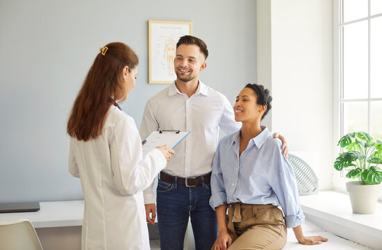 Multiethnic positive couple listening female doctor sharing health advices related to pregnancy, infertility, or reproductive health. Fertility, family planning consultation in clinic concept