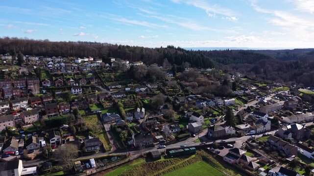 Drone aerial footage of Cinderford town in Gloucestershire, surrounded by the Forest of Dean, showing residential buildings, townscape, woodland, and rolling hills in a semi-urban rural landscape