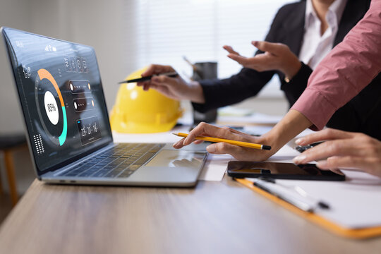 Professional engineers and business colleagues collaborating on project planning using a laptop with advanced digital dashboard interface, data analytics, and global logistics map in a modern office.