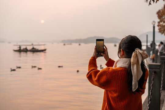 Young woman tourist taking photo of the sunset and scenic boat ride on the Xihu Lake in Hangzhou, China