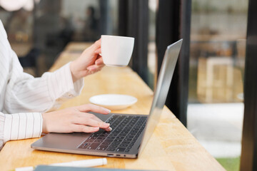 Fototapeta premium A woman is typing on a laptop while holding a cup of coffee. The scene suggests a busy workday, with the woman likely working on a project or responding to emails 