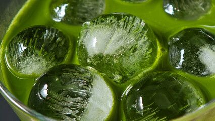 Vibrant green matcha latte being poured into a glass with ice cubes creating a refreshing