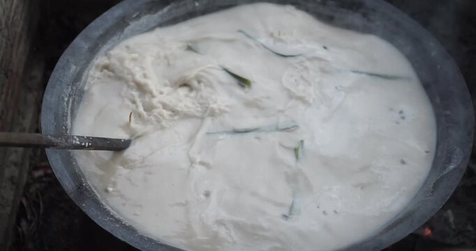 Boiling white liquid in a metal pot with a spoon inside.
