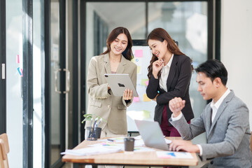 Fototapeta premium Group of young Asian professionals engaging in a dynamic brainstorming session. A female leader stands confidently while presenting ideas to her colleagues, showcasing a collaborative, positive
