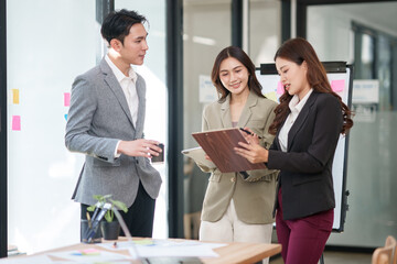 Fototapeta premium Group of young Asian professionals engaging in a dynamic brainstorming session. A female leader stands confidently while presenting ideas to her colleagues, showcasing a collaborative, positive