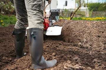 Organic farming man cultivates the ground with a tiller preparing the soil for sowing © erika8213