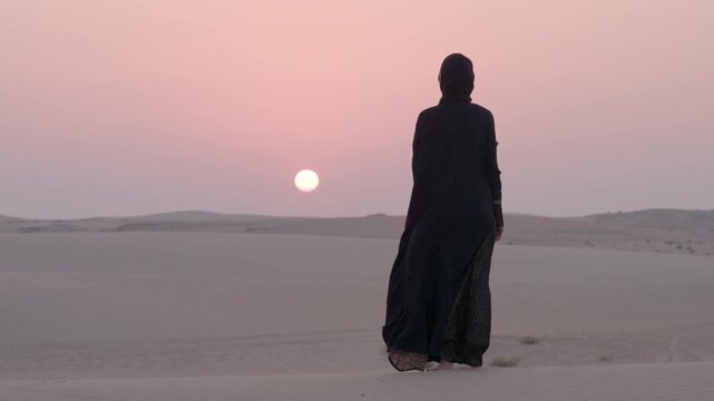  Arabic woman with Abaya cloth slow motion standing and looking at the  far distant remote desert with beautiful sand dune sunset during sunset