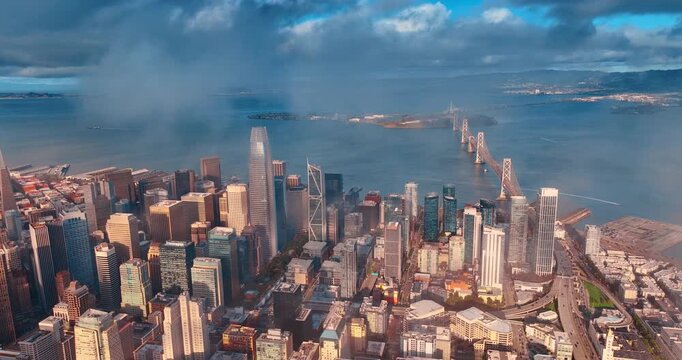 Flight in the clouds floating over downtown San Francisco, California, USA. View on the Oakland Bay Bridge over the bay with lively traffic.