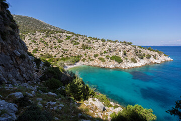 Fototapeta premium View of a small and idyllic beach in a cove surrounded by rugged and hilly coastline by the Aegean Sea on Kalymnos island in Greece on a sunny day.