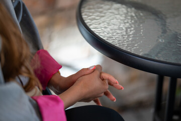 Woman hands with pink French manicure resting on lap beside a glass-top table.