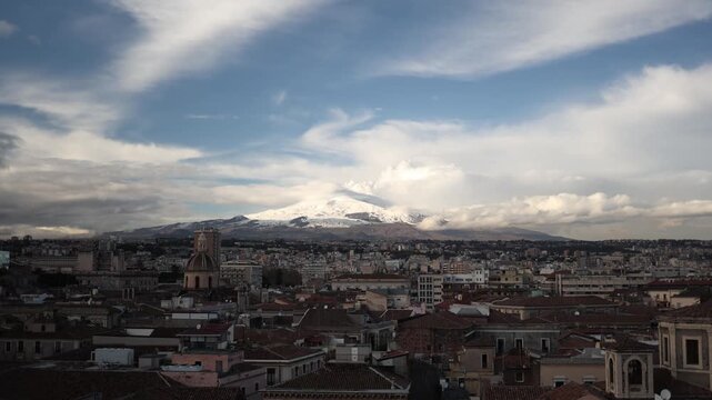 Mount Etna rising snow covered above Catania city rooftops dramatic clouds drifting over active volcano and Sicilian urban landscape panoramic Mediterranean view