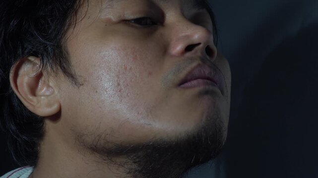 Extreme close up of a focused Asian man trimming his sideburns and beard with an electric clipper. Cinematic lighting highlighting skin texture, facial hair grooming, and masculine self-care routine i
