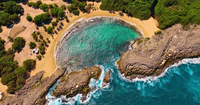 Top view of Mar Chiquita beach natural tide pool. Vertical aerial shot of a crescent-shaped natural pool protected by rock formations with turquoise water.