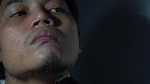 Close-up of a young Asian man shaving his beard and mustache using a manual razor and electric trimmer. Focus on skin care, grooming routine, and male hygiene in a home setting. Authentic daily life r