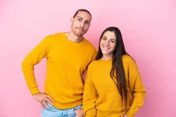 Fototapeta premium Young caucasian couple isolated on pink background posing with arms at hip and smiling