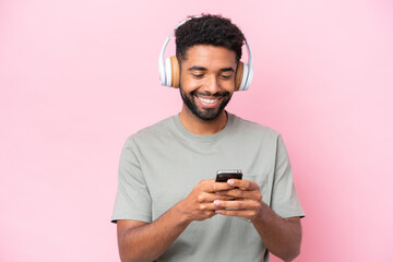 Fototapeta premium Young Brazilian man isolated on pink background listening music and looking to mobile