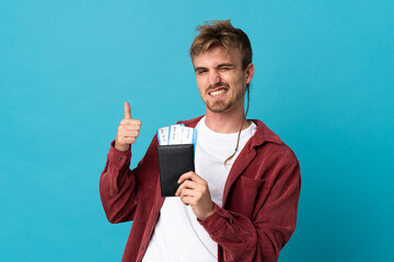 Young handsome blonde man isolated on blue background in vacation holding a passport and plane with...
